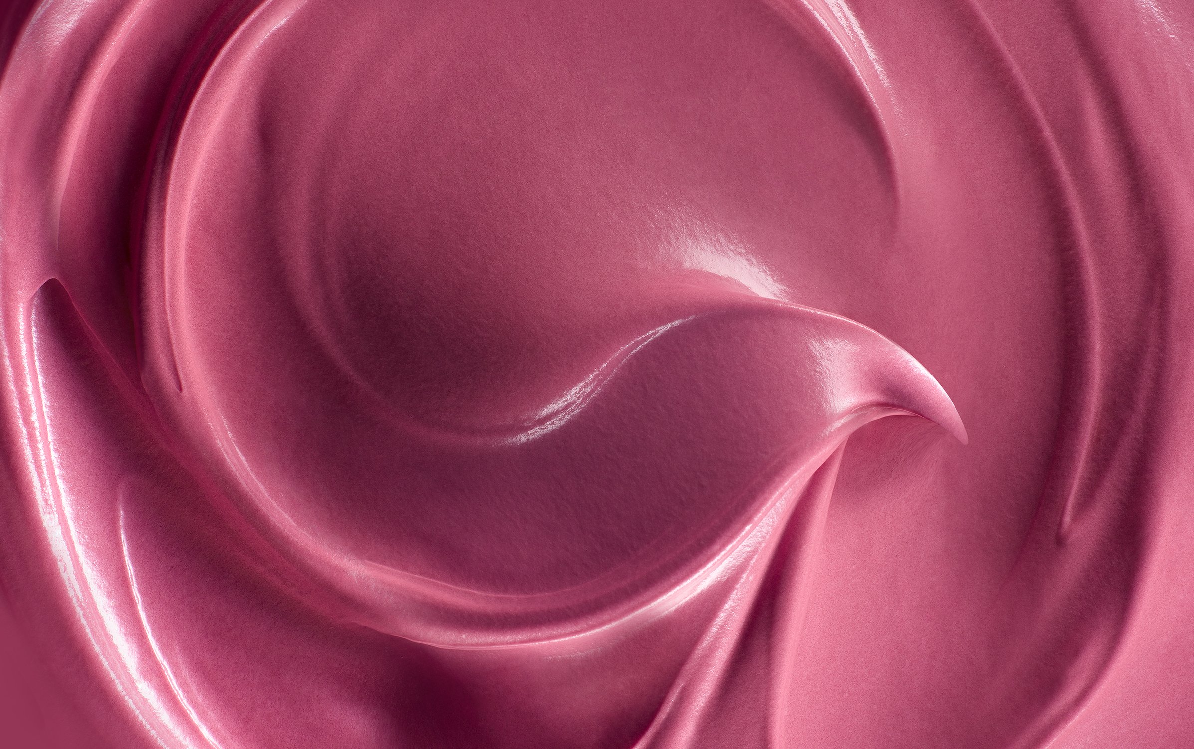 Close-up of a cosmetic product, showing swirling patterns and a smooth, shiny texture in shades of pink and rose, beauty product.