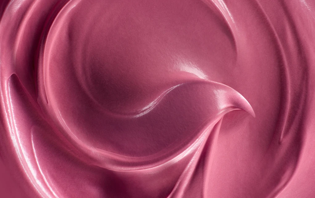 Close-up of a cosmetic product, showing swirling patterns and a smooth, shiny texture in shades of pink and rose, beauty product.