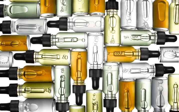 Overhead arrangement of glass dropper bottles filled with amber, green, and clear liquids on a white background