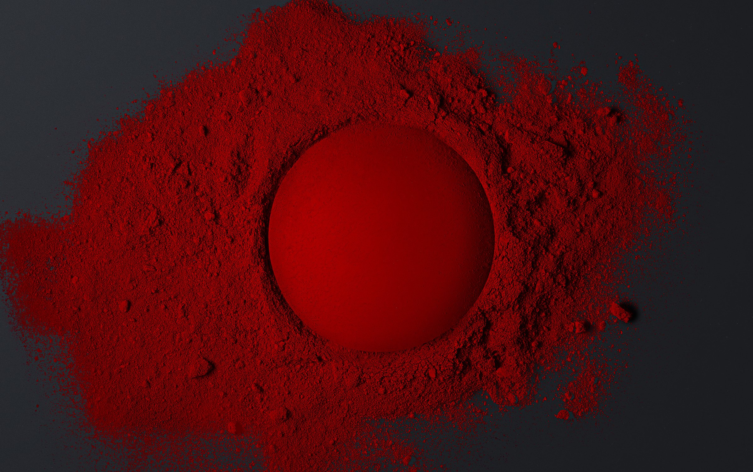 Red sphere centered in a field of vibrant red powder on a dark background, creating a striking contrast with texture and color.
