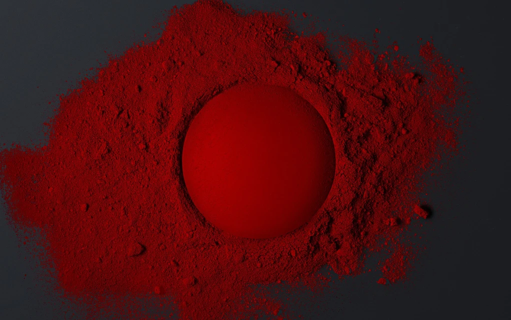 Red sphere centered in a field of vibrant red powder on a dark background, creating a striking contrast with texture and color.