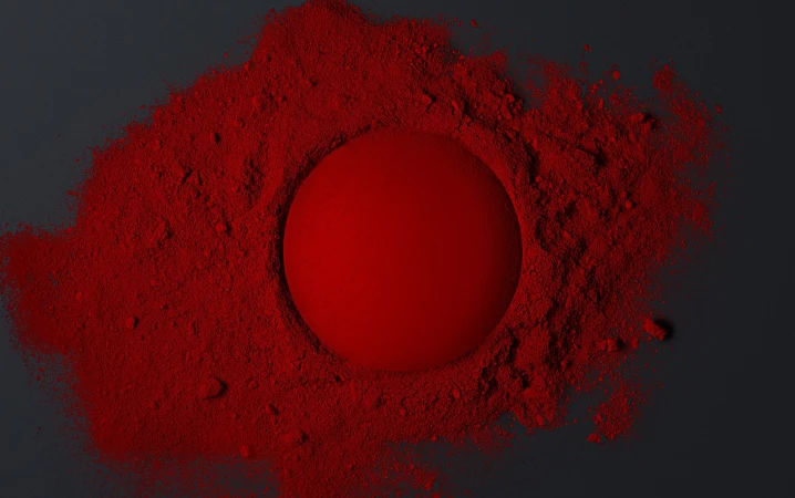 Red sphere centered in a field of vibrant red powder on a dark background, creating a striking contrast with texture and color.