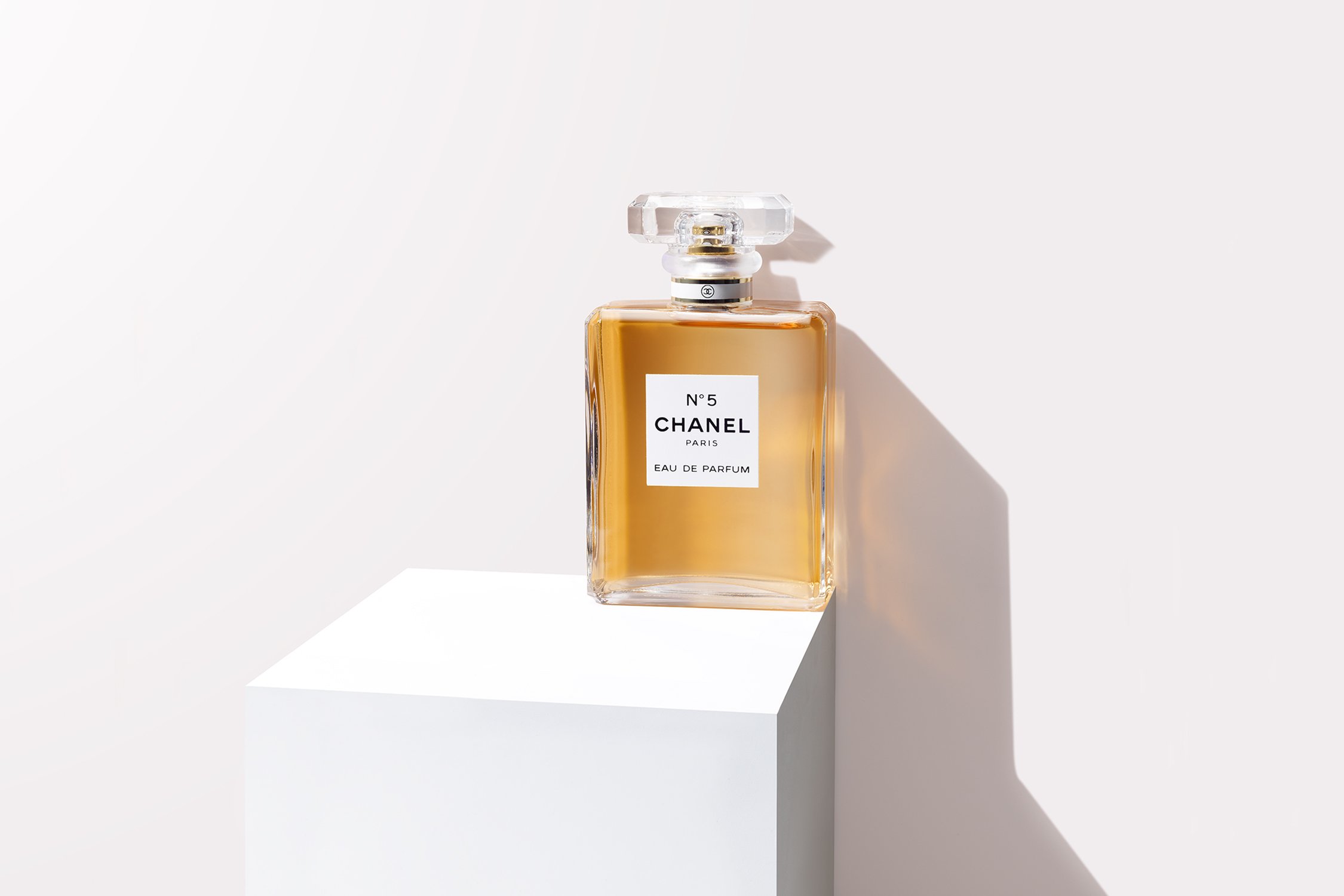 Chanel No. 5 perfume bottle on a white cubic stand against a bright white background, showcasing the product's design and elegance.