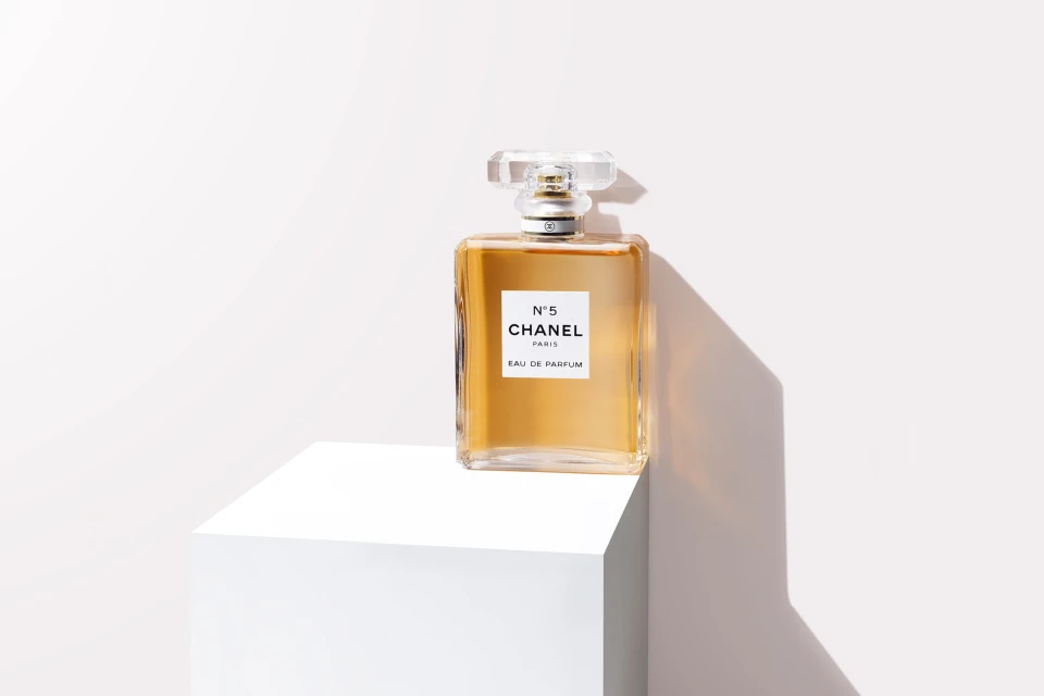Chanel No. 5 perfume bottle on a white cubic stand against a bright white background, showcasing the product's design and elegance.