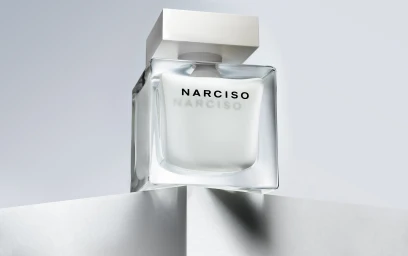 Square glass perfume bottle with a white square cap on an angular white pedestal against a neutral background