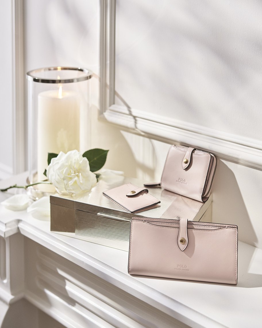 Elegant arrangement of pink leather wallets and cardholders displayed with a white rose and candle on a white surface, indoor setting.