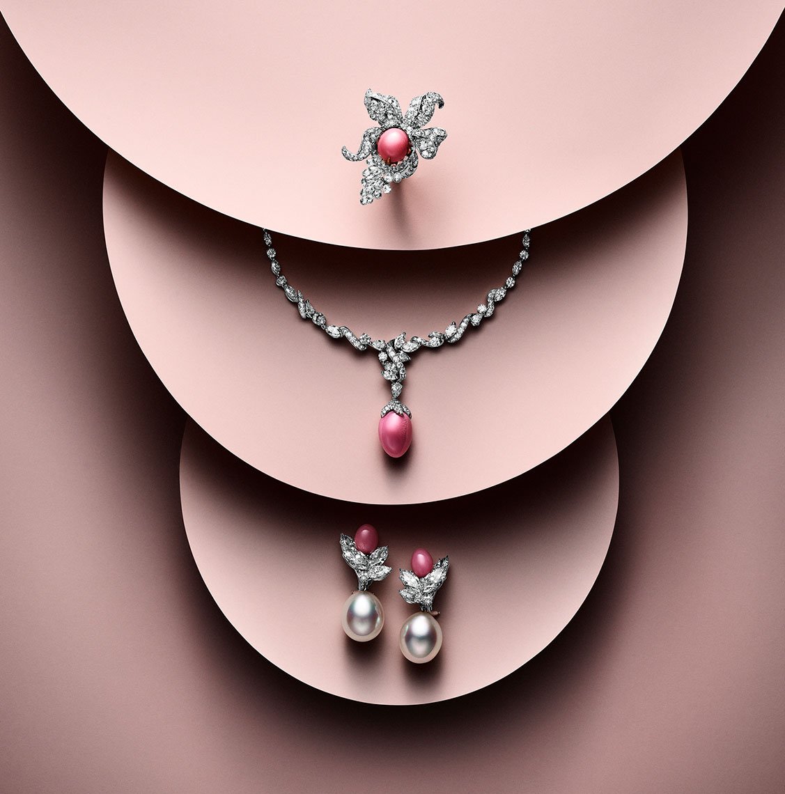 Elegant jewelry set featuring a necklace, earrings, and ring with pearls and diamonds displayed on a soft pink background.