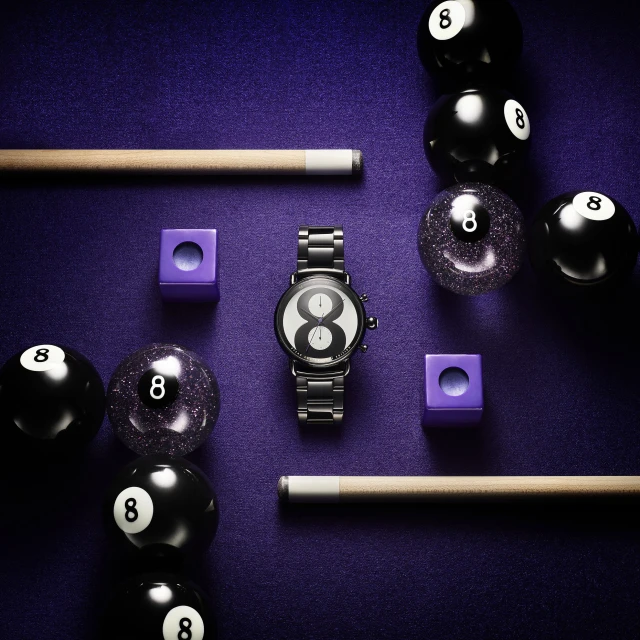 Wristwatch flat lay on purple surface, centered among billiard balls, chalk cubes, and cue sticks, showcasing a lifestyle product.