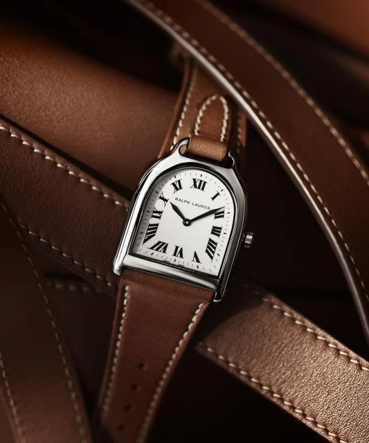 Elegant wristwatch with a white face, brown leather strap, and silver hardware, lying against a background of brown leather straps.