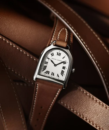 Elegant wristwatch with a white face, brown leather strap, and silver hardware, lying against a background of brown leather straps.