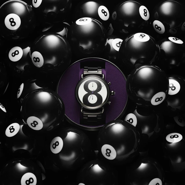 Elevated shot of a wristwatch with a black and white face displaying the number 8, displayed in the center of scattered 8-balls.