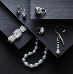 Collection of fine pearl and diamond jewellery including rings, earrings, and a multi-strand watch arranged on dark textured paper