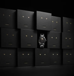 Black watch with gold accents positioned centrally amidst a grid of dark rectangular packaging boxes with gold cat eyes.