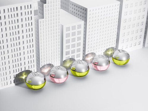 Eye-level shot of spherical containers with silver lids, some displaying pink bottoms and others showing yellow bottoms, against miniature white buildings.