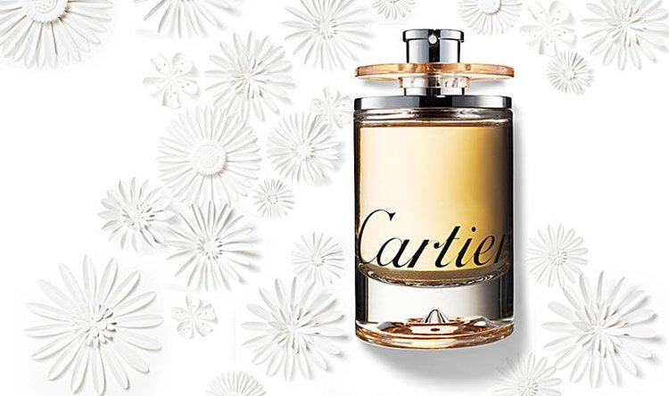 Elegant close-up of a Cartier perfume bottle with a golden liquid inside and white daisy decorations on a bright, clean background.