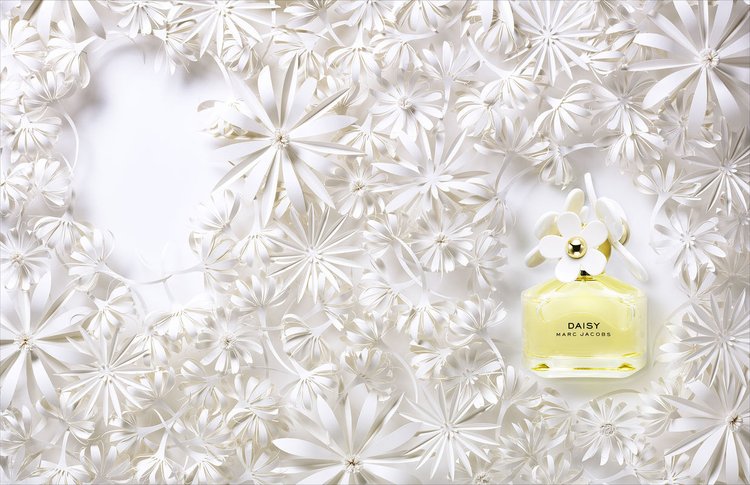 Perfume bottle surrounded by paper flowers in a studio setting, showcasing a delicate and artistic floral arrangement.