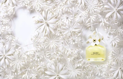 Marc Jacobs Daisy perfume bottle surrounded by intricate white paper craft flowers