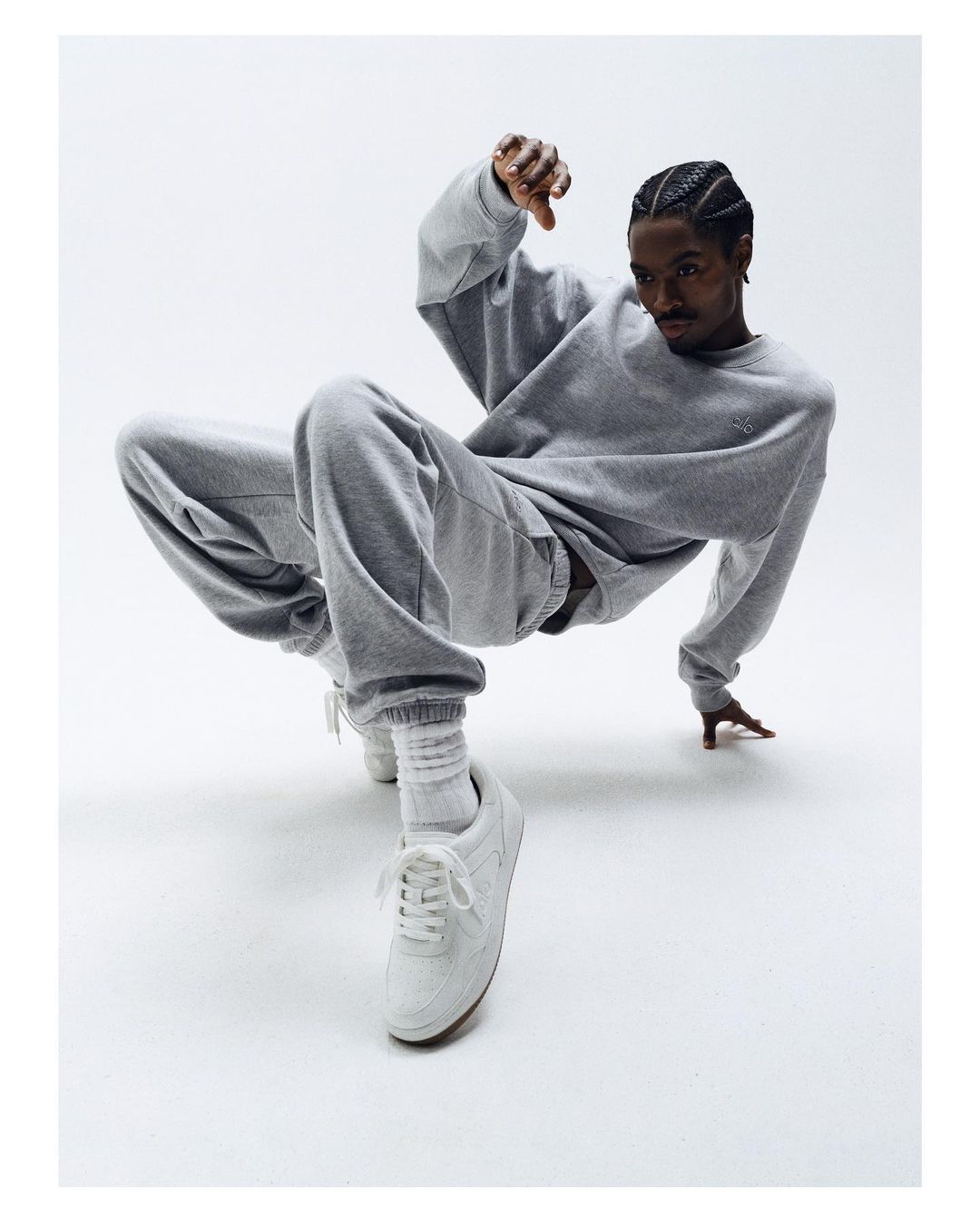 A man in a grey tracksuit strikes a dynamic pose against a bright backdrop, showcasing fashion and athleticism with a clear and crisp visual focus.