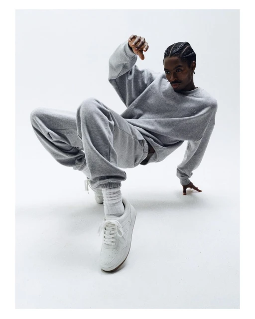 A man in a grey tracksuit strikes a dynamic pose against a bright backdrop, showcasing fashion and athleticism with a clear and crisp visual focus.