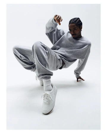 A man in a grey tracksuit strikes a dynamic pose against a bright backdrop, showcasing fashion and athleticism with a clear and crisp visual focus.