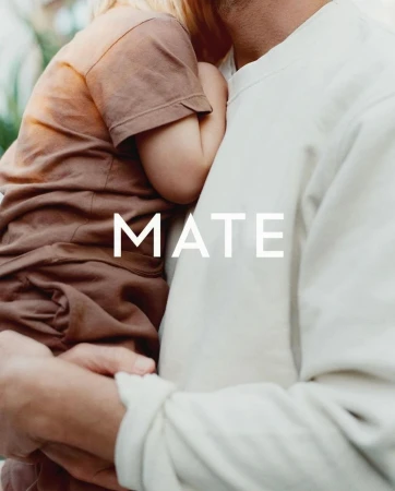 Adult holding a small child wearing brown clothing with the word MATE overlaid