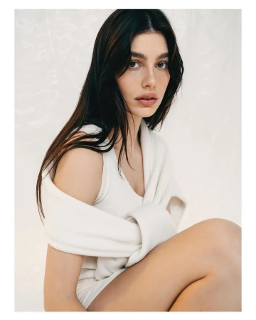 Portrait of a woman with dark hair in a white knit top shot against a pale textured background by Bryan Rodner Carr