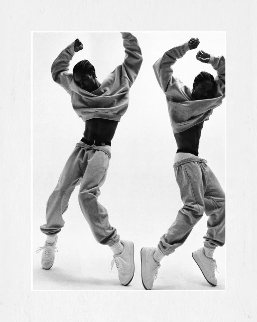 Monochrome photo of African American man jumping in grey sweatsuit, captured twice with arms raised, white background, fashion editorial.