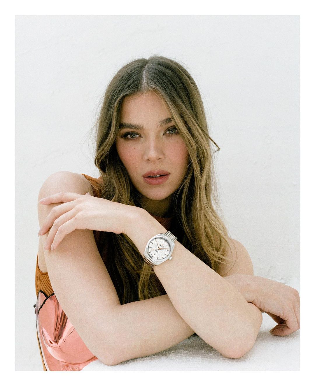 Portrait of a woman with long blonde hair wearing a silver wristwatch, shot in a bright photo studio with a light background.