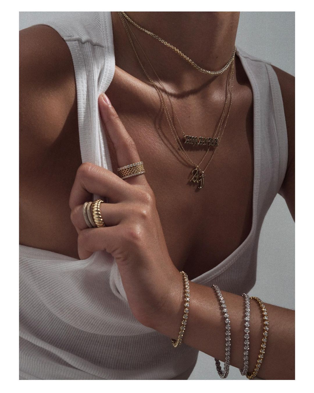 Close-up shot of a woman's hand and wrist adorned with rings and bracelets, set against a white tank top, highlighting jewelry details.