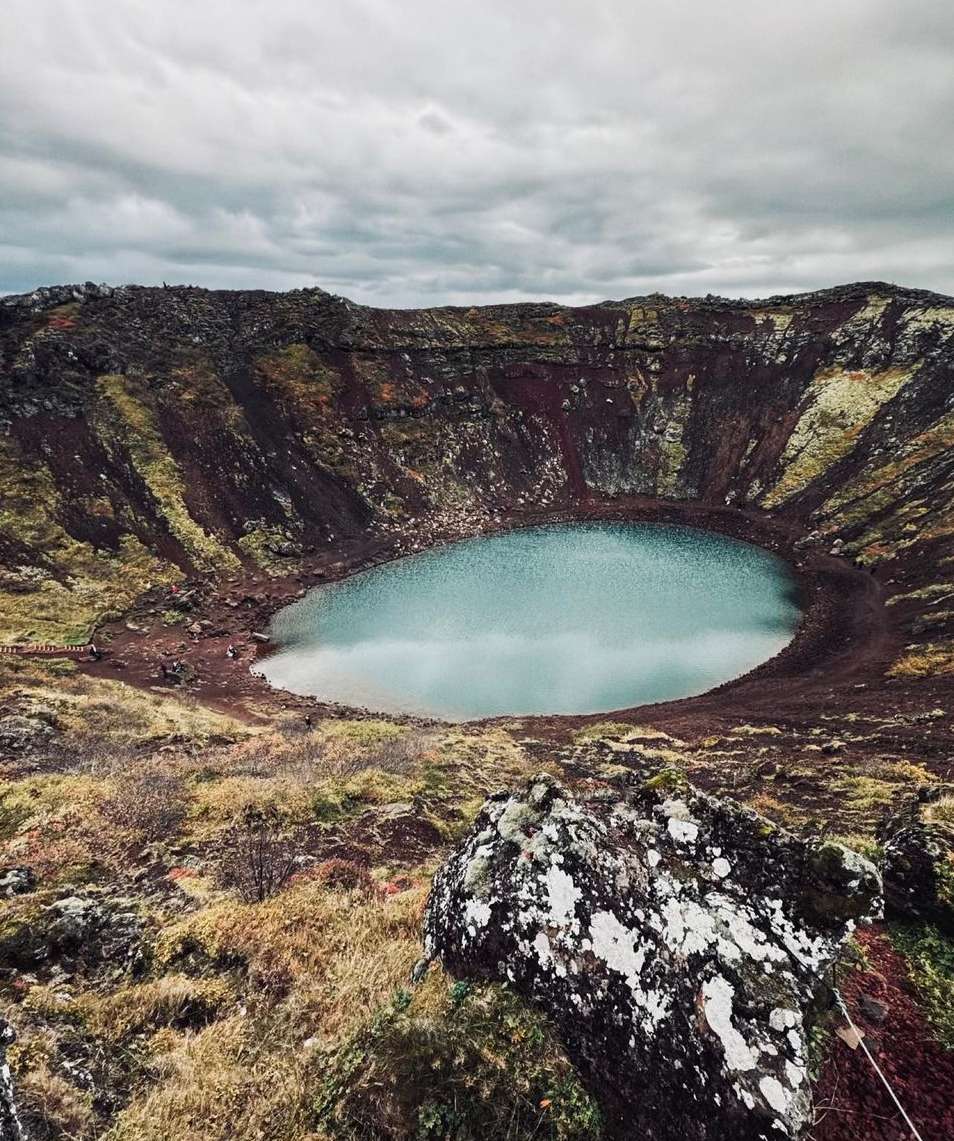 Crater lake landscape in Iceland with blue water, brown volcanic rock, and moody sky. Serene travel destination in nature.