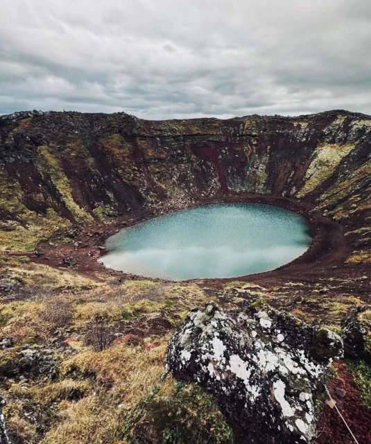 Crater lake landscape in Iceland with blue water, brown volcanic rock, and moody sky. Serene travel destination in nature.
