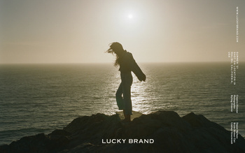 Woman on rocky cliff overlooking ocean at sunset in an outdoor fashion shot for Lucky Brand apparel. Tranquil scene.