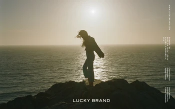 Woman on rocky cliff overlooking ocean at sunset in an outdoor fashion shot for Lucky Brand apparel. Tranquil scene.