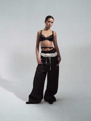 Fashion shot of an adult woman in a bra top and baggy pants posing in a photo studio against a neutral gradient backdrop.