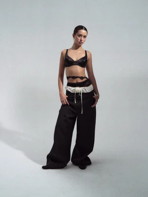 Fashion shot of an adult woman in a bra top and baggy pants posing in a photo studio against a neutral gradient backdrop.