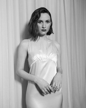 Portrait of a woman with short dark hair in a satin dress standing against draped fabric curtains in a monochrome image