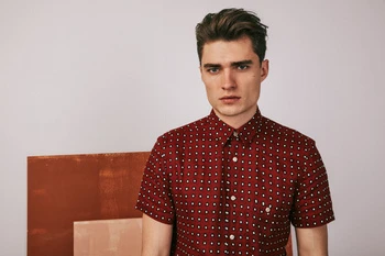 Studio shot of a dark-haired adult male model wearing a short-sleeved red and white patterned shirt against a neutral background.
