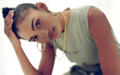 Portrait of a black woman with gold hoop earrings wearing a green tank top against a white background by Bryan Rodner Carr