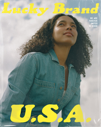 Portrait of a woman with curly hair wearing a denim jumpsuit against a cloudy sky with yellow typography