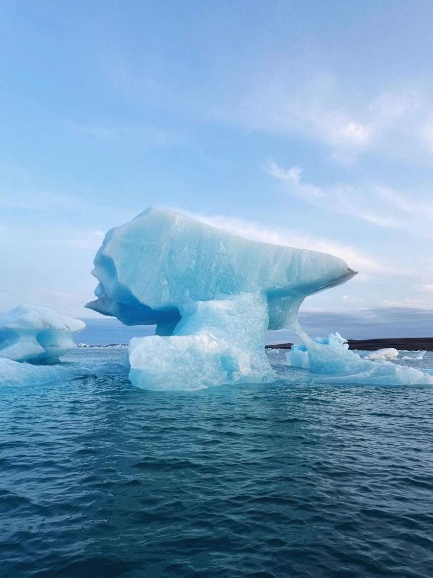 Icebergs in the Jokulsarlon glacier lagoon in Iceland feature blue ice formations floating on dark blue water under a blue sky.