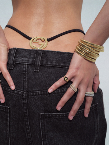 Close-up of an adult female's lower back wearing black jeans and gold bracelets and rings, showcasing fashion and accessories.