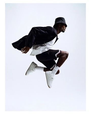 Full body shot of an adult male in mid-air wearing casual clothes, a bucket hat, jacket, shorts, socks, and sneakers, against a white background.