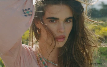 Close-up portrait of a woman in a pink embroidered top with gold hoop earrings and beaded necklaces outdoors in Los Angeles.