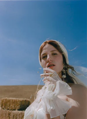 Low angle portrait of a woman wearing a white headscarf and sheer gloves against a clear blue sky