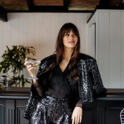 Woman in a black sequin outfit holding a martini glass while leaning against a dark bar counter in Los Angeles.