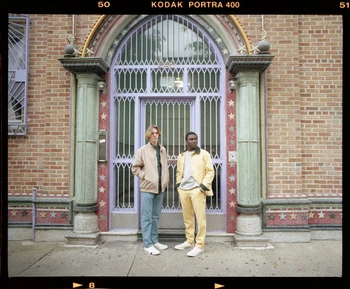 Two young men standing in front of an ornate purple doorway with columns and red brick facade shot on film