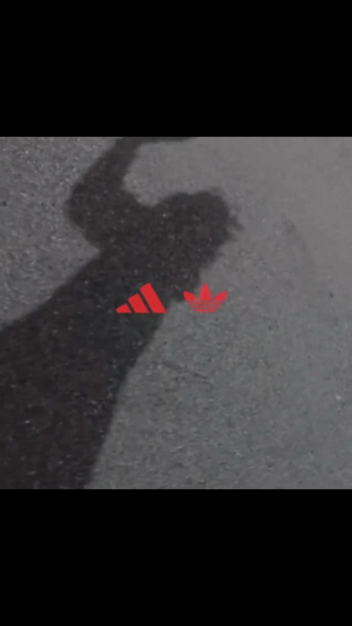 Shadow of a person on a street with red Adidas logos on the ground, creating a minimalist and artistic street scene.