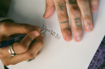 Close-up of hands writing calligraphy on white paper with a fountain pen, displaying precision and artistry.