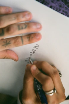 Close-up of hands writing calligraphy on white paper with a fountain pen, displaying precision and artistry.