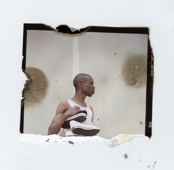 Black man holding white sneakers against a textured backdrop within a distressed polaroid frame format.